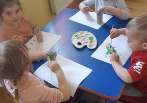 Dzieci malują farbami rolkę po papierze toaletowym.